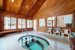 A wooden interior with a pool, benches, and plastic chairs.