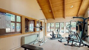 Et fitnesscenter med forskellig træningsudstyr, store vinduer og loft af træ.