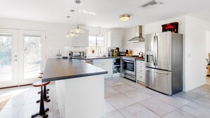Een moderne keuken met een groot eiland, roestvrijstalen apparatuur en hangende lampen.