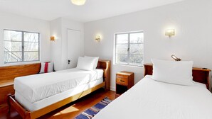 Een slaapkamer met twee enkele bedden, een houten bankje, een klein nachtkastje en een raam met uitzicht.