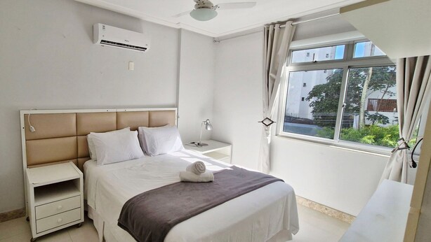 A bedroom with a bed, bedside table, nightstand, and an air conditioning unit. - COAPI0100 - Edificio Palais Atlantique (Salvador)