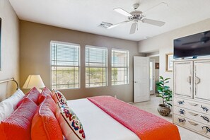 Ein Schlafzimmer mit einem Bett, einem Deckenventilator, einem Fernseher und einem Fenster mit Jalousien.