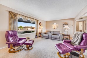 Ein Wohnzimmer mit einer Couch, zwei Schaukelstühlen, einer Lampe und Blick auf Palmen.