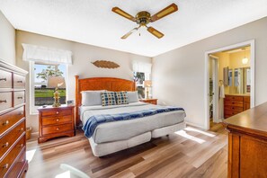 Une chambre à coucher avec un lit en bois, une table de chevet, une commode et un ventilateur de plafond.
