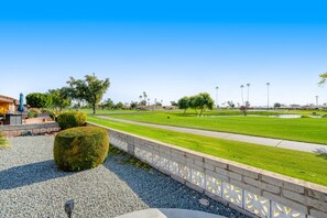 Ein gepflegter Park mit einem gepflasterten Weg, ordentlich geschnittenen Hecken und einem klaren, blauen Himmel.