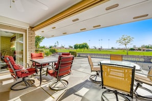 Une terrasse extérieure avec une table et des chaises en verre, une vue sur un terrain de golf et un mur en briques.