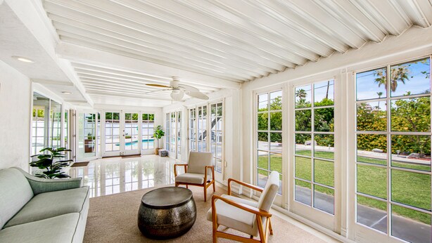 A spacious room with a large window, a ceiling fan, and a sofa. - Appealing Racquet Club home with firepit, private pool & gas grill (Palm Springs)