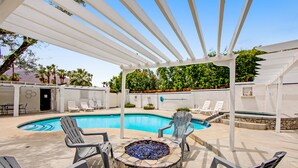 A pool area with a stone fire pit, lounge chairs, and a pergola. - Appealing Racquet Club home with firepit, private pool & gas grill (Palm Springs)