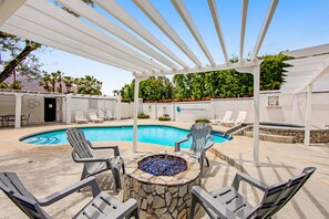 Ein Poolbereich mit Feuerstelle aus Stein, Liegestühlen und einer Pergola.