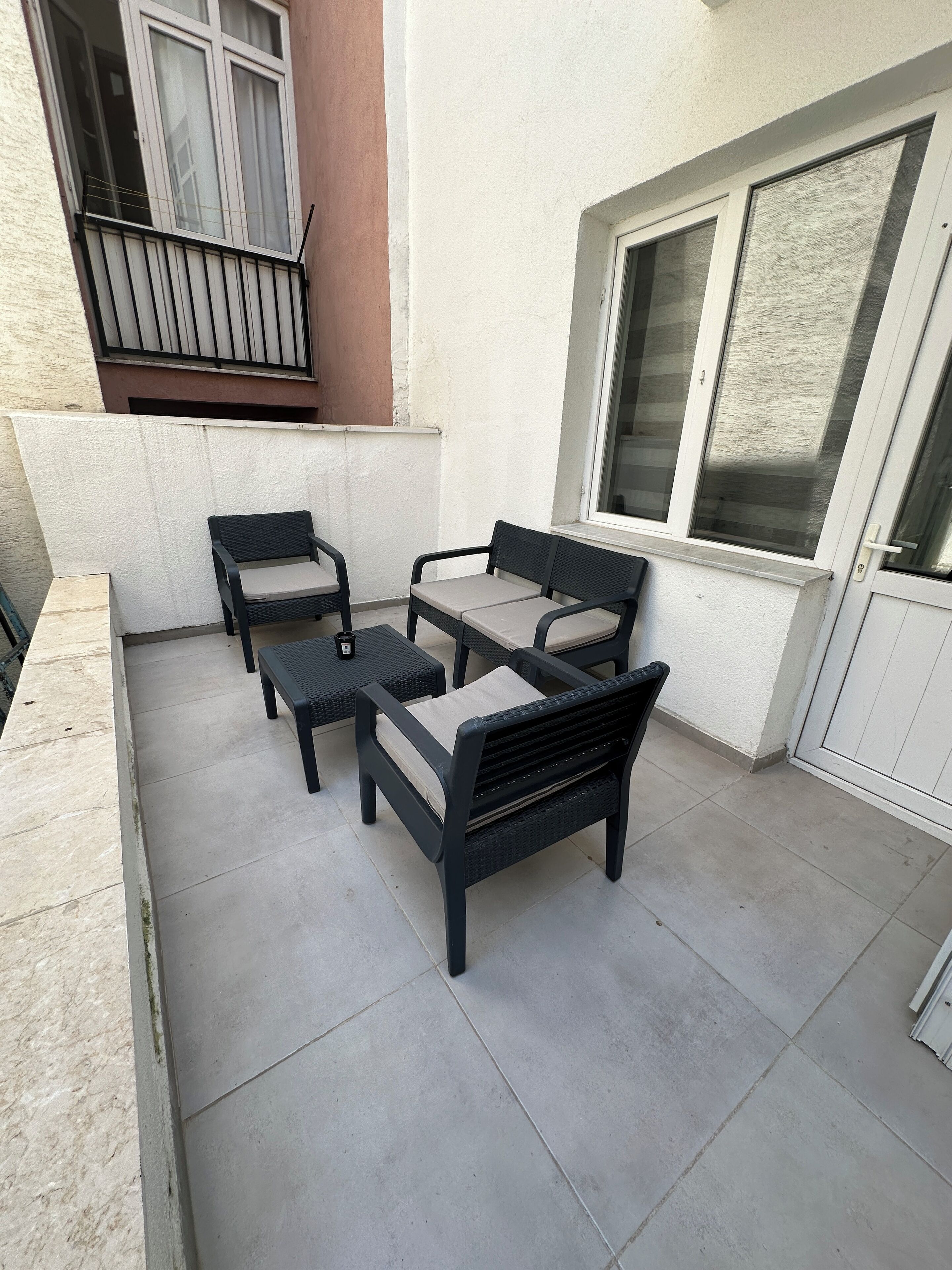 A patio area with a seating arrangement consisting of a sofa and two chairs, a small table, and a window with blinds.