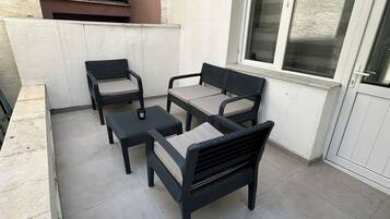 A patio area with a seating arrangement consisting of a sofa and two chairs, a small table, and a window with blinds.