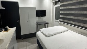 Une chambre moderne équipée d’un lit, d’un bureau, d’une télévision et d’une armoire.