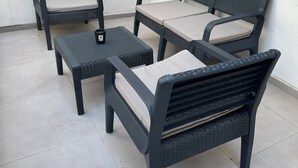 Une terrasse agrémentée d'un ensemble composé de quatre chaises en osier noir et d'une table assortie, chacune étant dotée d'un coussin de couleur claire.