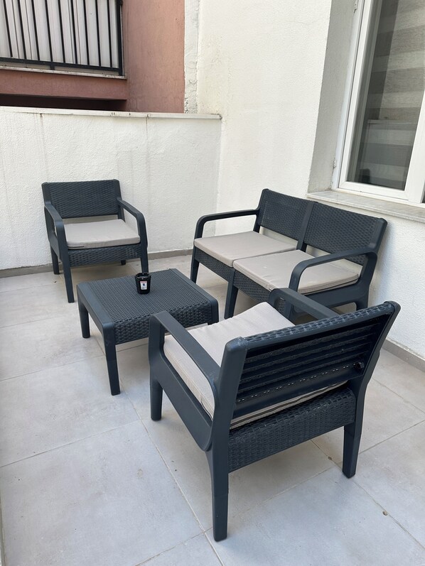 A patio with a set of four black wicker chairs and a matching table, each with a light-colored cushion.