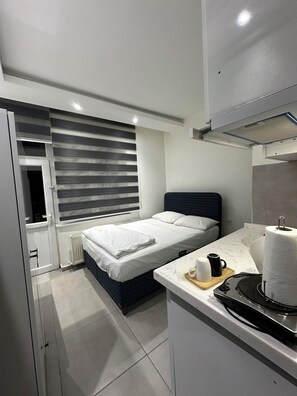 A modern bedroom with a bed, bedside table, and a window with blinds.