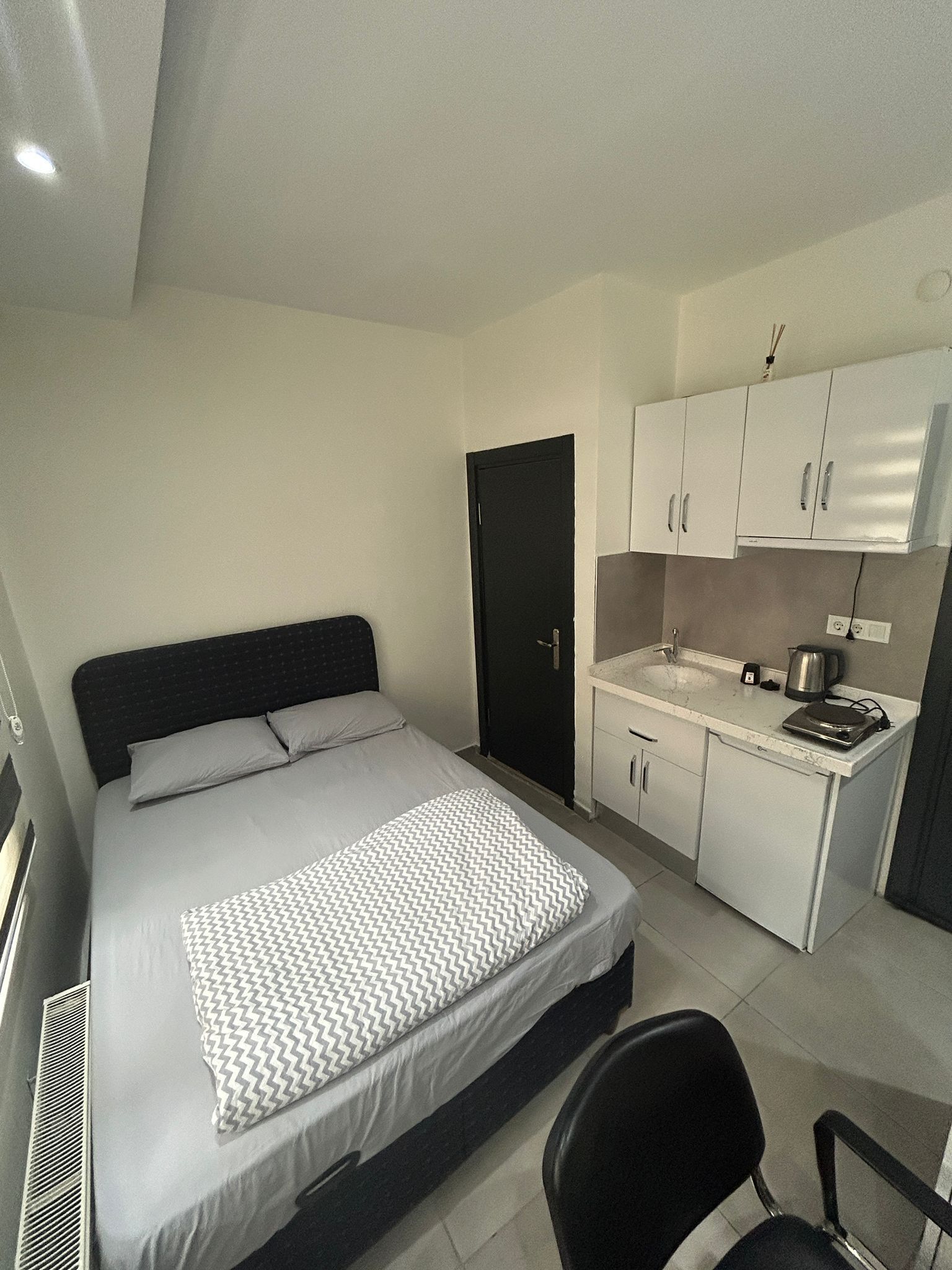 Une chambre compacte comprenant un lit, une petite kitchenette et une porte.