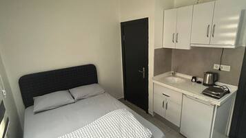Une chambre compacte comprenant un lit, une petite kitchenette et une porte.