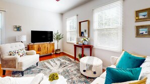 Una sala de estar con sofá, reposapiés y televisor sobre un mueble de madera.