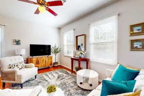 A living room with a sofa, ottoman, and a television on a wooden cabinet. - Classy house near trails with pools, playground, basketball & beautiful upgrades (Gilbert)