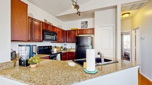 Una cocina con encimeras de granito, armarios de madera, un refrigerador negro y una lámpara en el techo.