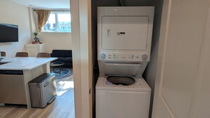 Un lavadero pequeño con lavadora y secadora, una cocina compacta con lavavajillas, y un comedor con mesa y sillas.