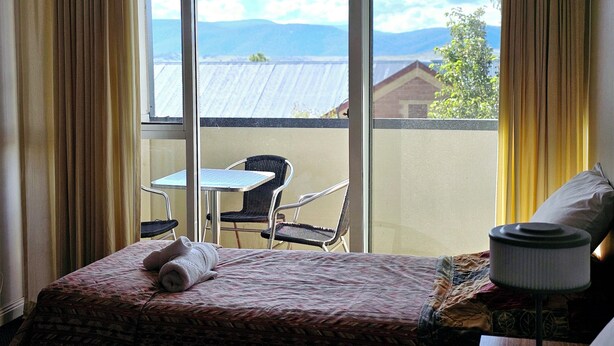 Habitación de hotel con cama, una mesita, una silla y vistas al exterior.