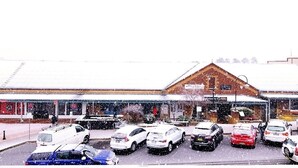 Un edificio con techo nevado y un estacionamiento con varios coches.