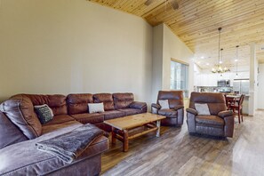 Un vaste salon doté d’un plafond en bois, de canapés en cuir, d’une table basse en bois et, au fond, d’un coin repas.