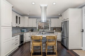A modern kitchen with white cabinets, a stainless steel refrigerator, and a central island with two wooden chairs.