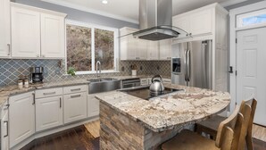 Una cocina moderna con armarios blancos, una isla de granito, electrodomésticos de acero inoxidable y un amplio ventanal.