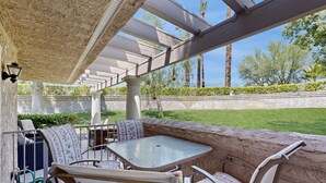 Un patio al aire libre con mesa y sillas, una pérgola y vista a un área verde con árboles.