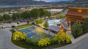 A tennis court, a pool, and a building with a unique architectural design. - Peaceful Garden Retreat with Family & Resort Amenities (West Kelowna)
