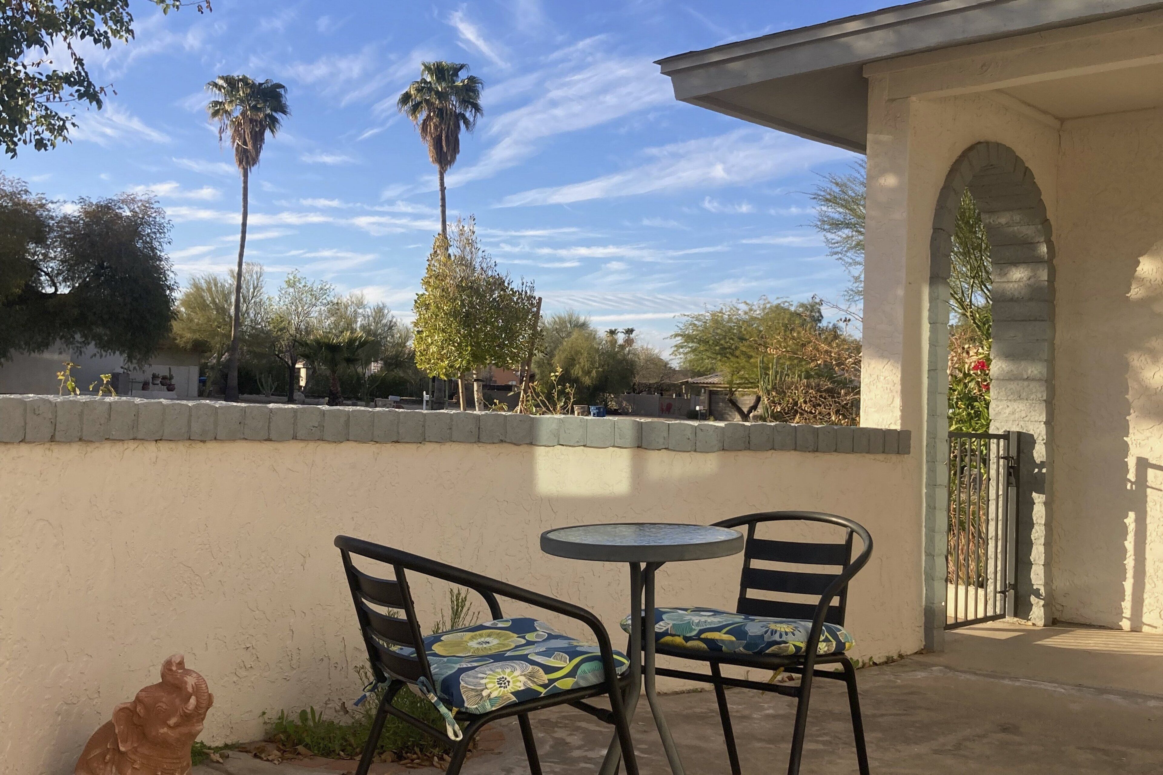 A patio with two chairs and a table, a stone wall, and a palm tree in the background.