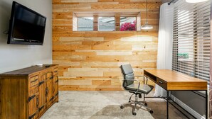 A modern room with a wooden wall, a desk, a chair, a television, and a window with blinds. - Snowbird-Friendly Home with Private Pool, Grill, AC, Fireplace, & WiFi - Dogs OK (Glendale)