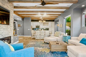 A modern living room with a fireplace, blue and white furniture, and a kitchen in the background.