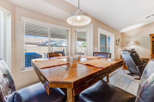 A dining area with a large wooden table, black leather chairs, and a ceiling light. - Lovely getaway with private pool, putting green & desk (Gilbert)