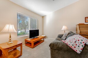A living room with a television on a wooden stand, a sofa, two lamps, and a window with blinds. - Lovely getaway with private pool, putting green & desk (Gilbert)