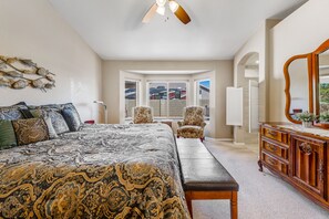 Une chambre avec un grand lit, un banc, une commode et une chaise. Il y a une fenêtre donnant sur un parking.