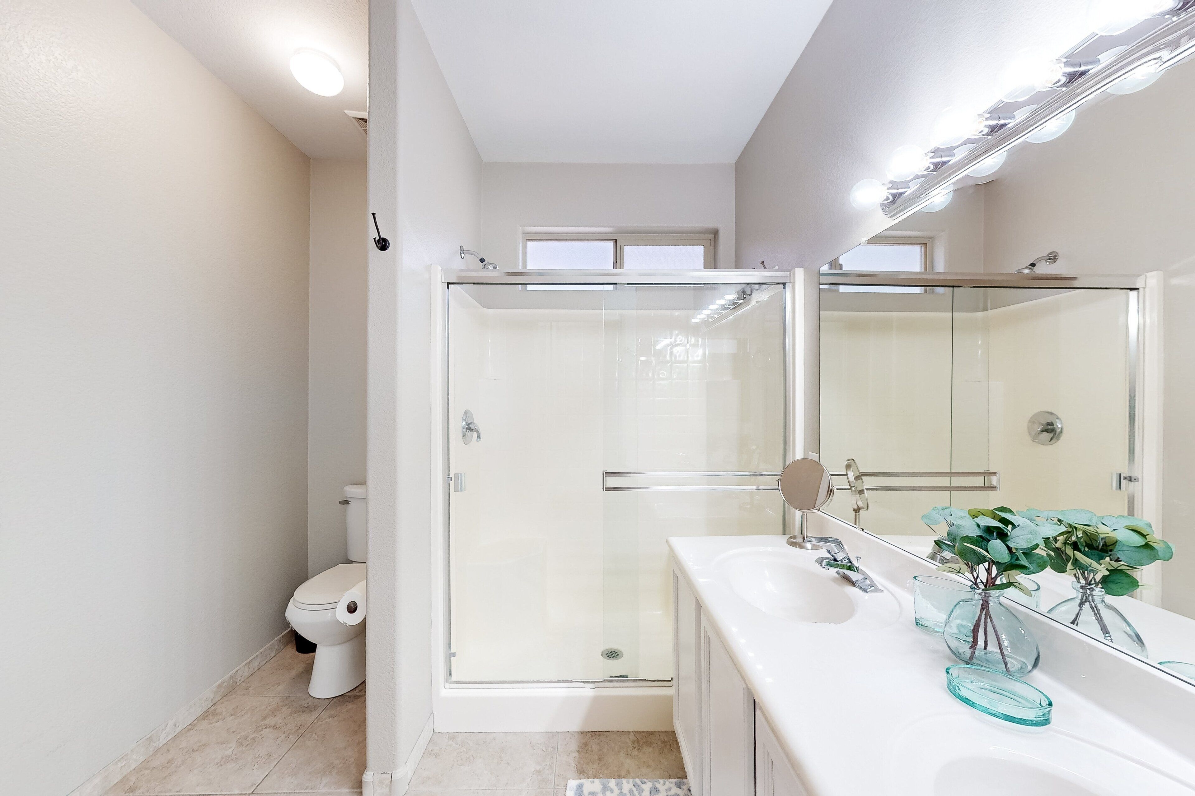 A modern bathroom with a glass-enclosed shower, a white toilet, and a vanity with a mirror and decorative vases.