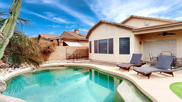 A poolside area with a house, a pool, and lounge chairs.