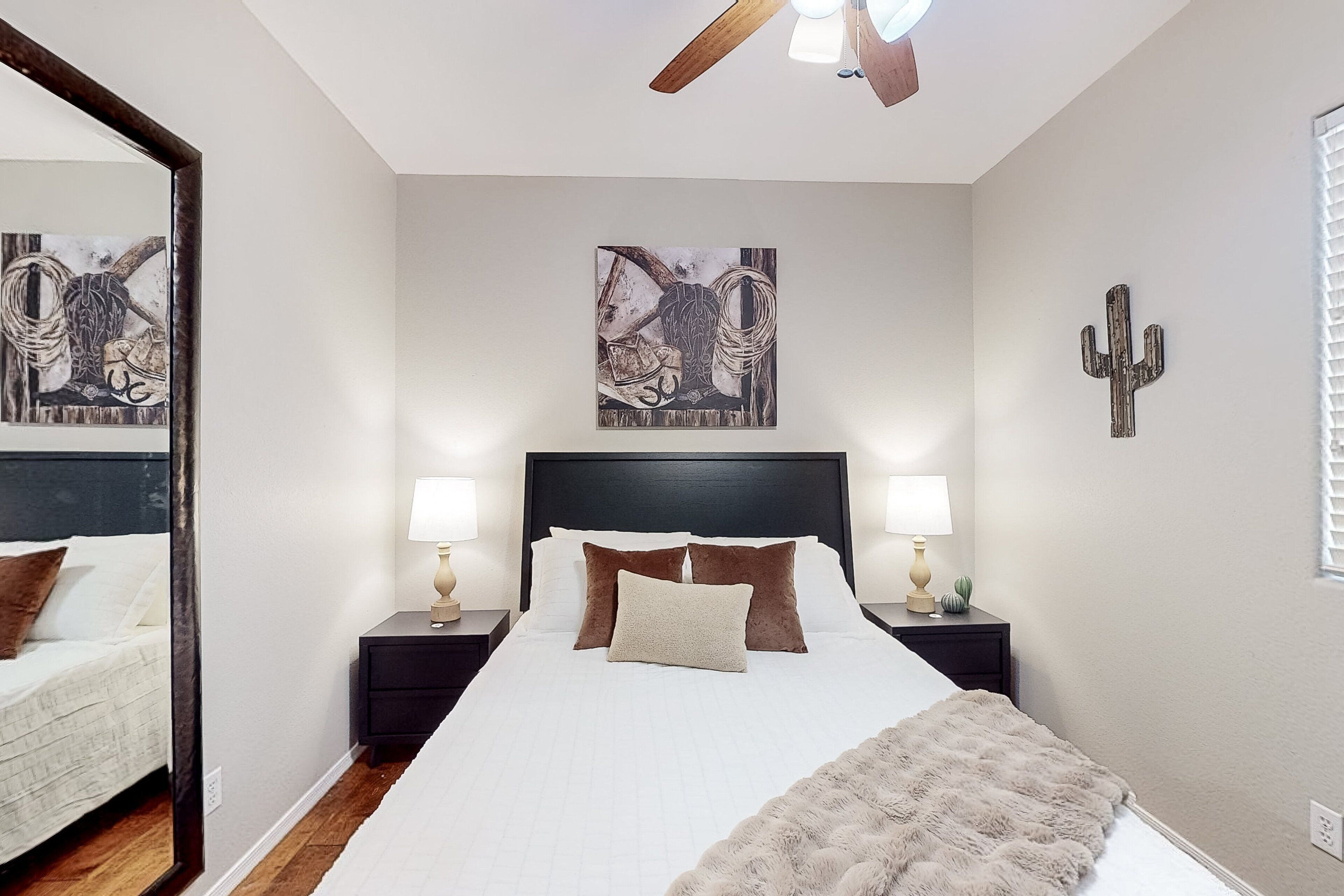 A bedroom with a large bed, two nightstands, a ceiling fan, and artwork on the walls.