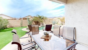 A patio with a glass table and chairs, a small potted plant, and a view of a swimming pool and desert landscape.
