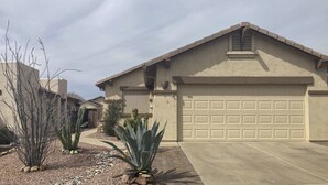 A residential house with a garage, a driveway, and desert plants.