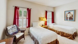 Une chambre avec deux lits simples, une chaise en osier, une petite table avec une lampe et un tableau au mur.