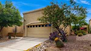 Un immeuble résidentiel doté d’un garage, entouré d’une végétation désertique comprenant des cactus et des arbres.