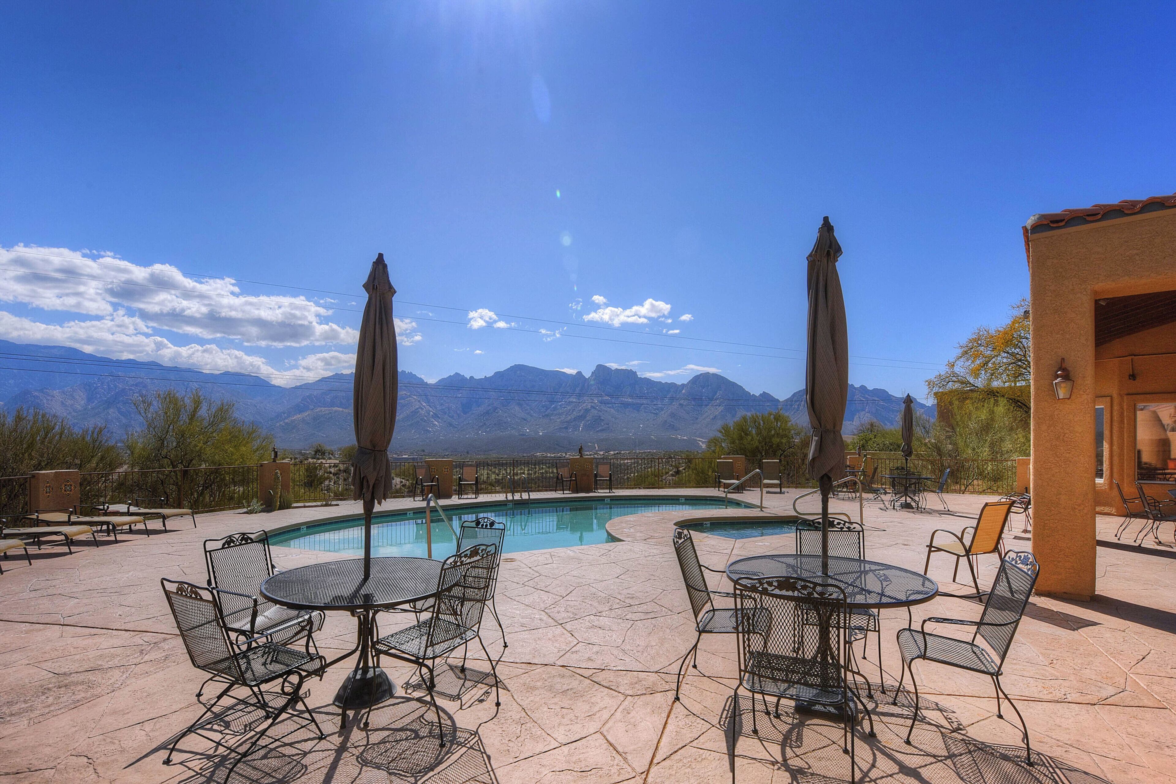 An outdoor pool area with tables and chairs, surrounded by mountains.