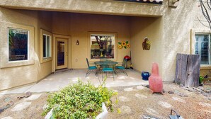 Une terrasse couverte avec une table et des chaises, une plante en pot et un vase rouge.