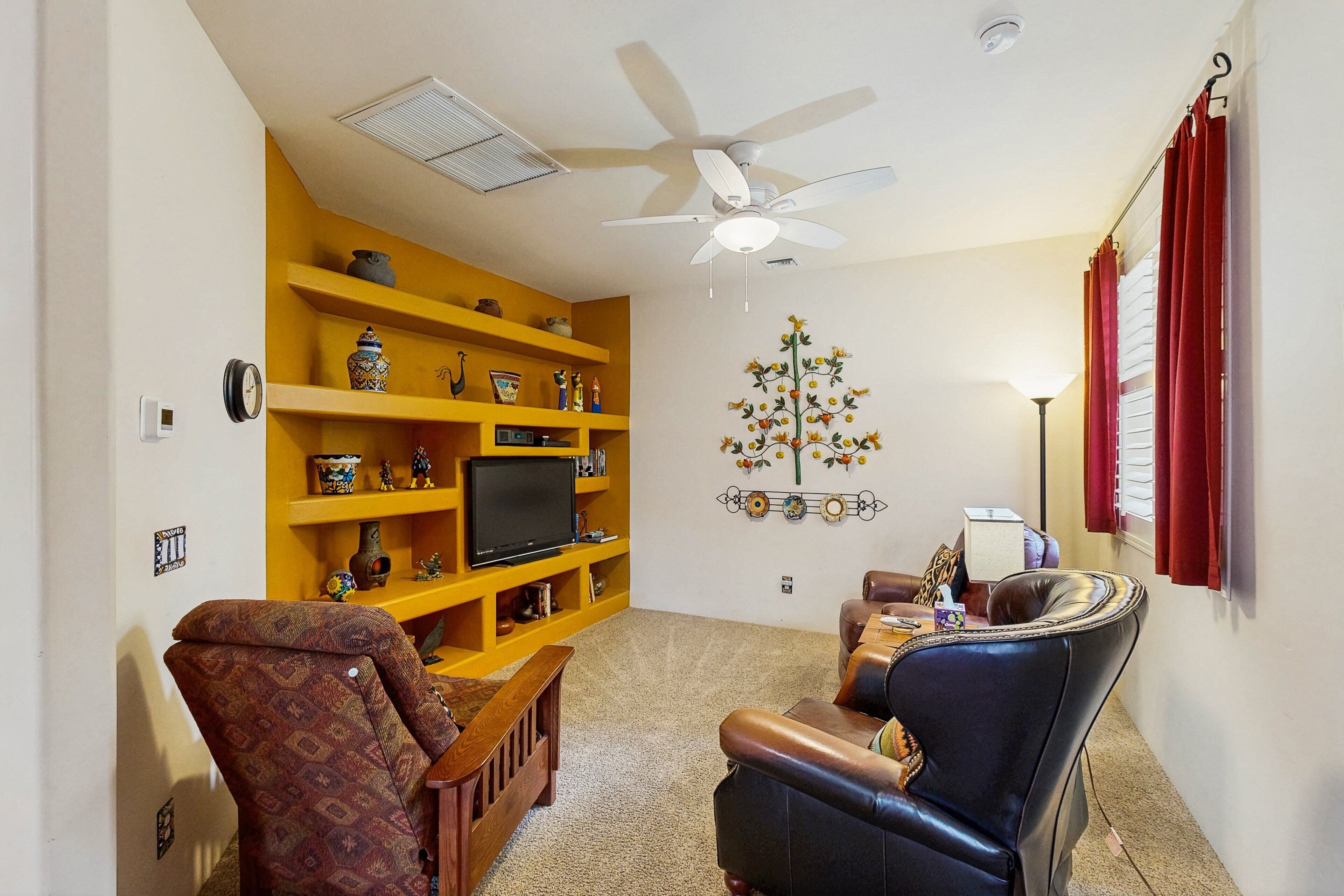 Un salon avec une bibliothèque jaune, un téléviseur, un ventilateur de plafond et un élément décoratif mural.