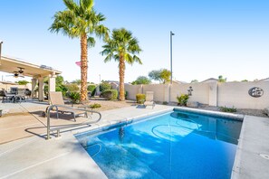 A swimming pool with a palm tree, a covered patio, and a wall with a circular emblem. - Dog-friendly home with pool, firepit, fast WiFi, central AC, & washer/dryer (Goodyear)