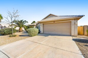 A residential driveway leading to a garage with a tiled roof, surrounded by landscaping and a clear sky. - Dog-friendly home with pool, firepit, fast WiFi, central AC, & washer/dryer (Goodyear)